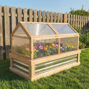 Wooden cold frame with transparent roof on grass, wooden fence in background
