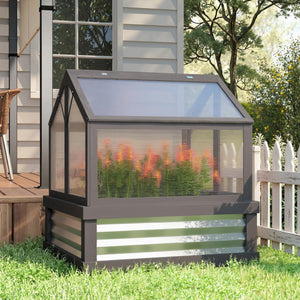 Small greenhouse with plants inside, attached to a house with a garden in the background.