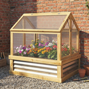 Wooden cold frame with plants against a brick wall
